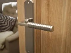 Poignée de porte d'entrée en métal brossé, au design moderne avec un manche texturé, fixée sur une porte en bois clair.