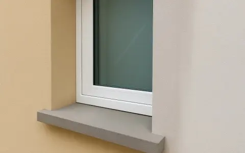 Une pose fenêtre sur appui de fenêtre en pierre grise, avec un mur extérieur texturé beige et un mur blanc cassé.