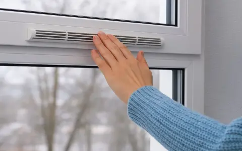 Main tenant ajuste la ventilation d'une fenêtre pour un confort optimal, même par temps froid.