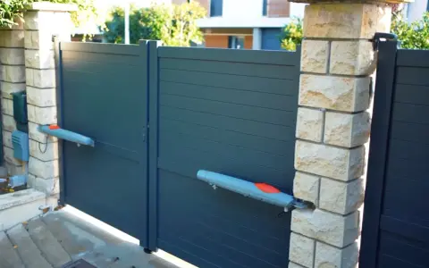 Portail gris moderne avec motorisation portail vérin ou vis sans fin. Deux bras gris et orange sont fixés sur les battants.