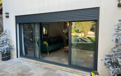 Volet battant alu RAl 7016, moderne, protégeant une baie vitrée donnant sur un salon et une piscine.