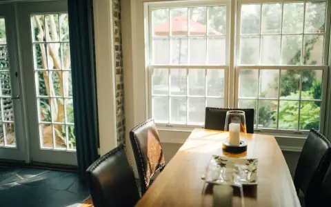 Le **couleur encadrement fenêtre intérieur** blanc met en valeur la lumière naturelle baignant la salle à manger. Des chaises en cuir marron entourent une table en bois.