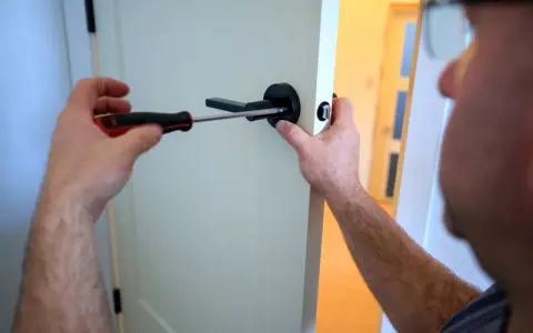 Un homme utilise un tournevis pour changer le ressort de rappel d'une poignée de porte noire.