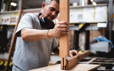 Artisan assemble des pièces de bois pour fabriquer une fenêtre. Il tient une pièce verticale et la joint à une autre pièce.