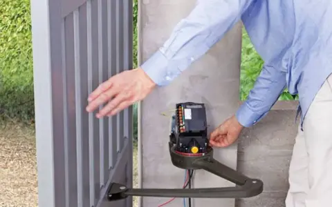 Un homme ajuste le moteur d'un portail électrique bloqué ouvert.
