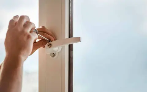 Main tenant utilise un tournevis pour changer la poignée d'une fenêtre en aluminium.