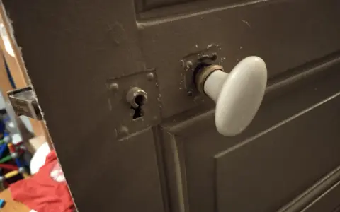 Détail du mécanisme poignée porte ancienne avec une rosace et une serrure visible.