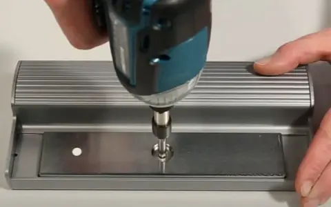 Utilisation d'une visseuse pour fixer une plaque métallique, étape clé pour ouvrir une porte aimantée.