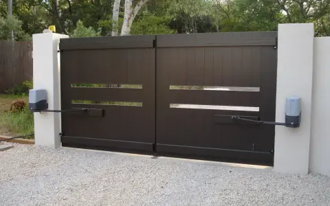 Portail dea bloqué, avec ses moteurs électriques fixés aux piliers blancs. Un chien brun se repose à l'extérieur.