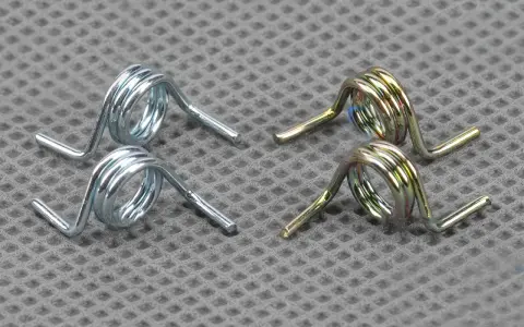 Deux ressorts argentés et deux ressorts dorés, essentiels au mécanisme d'une serrure de portail, reposent sur une surface texturée.