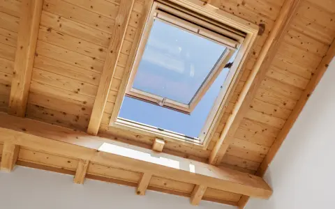 Un *uw velux* ouvert sur un ciel bleu éclatant, encadré par des poutres et un plafond en bois chaleureux.