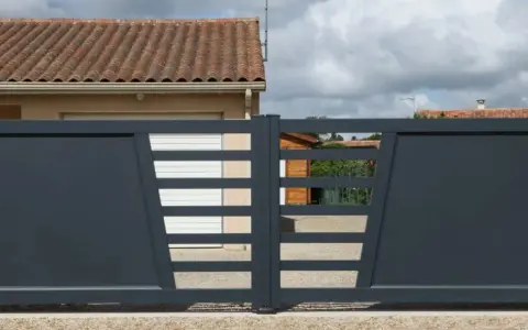 Portail solaire ne fonctionne plus. La grille grise moderne, avec ses lames horizontales et son design asymétrique, est fermée devant une maison.