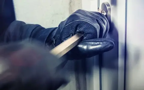 Main gantée utilise un pied-de-biche pour forcer une porte. L'effraction porte ses fruits.