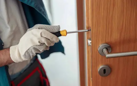 Main tenant utilise un tournevis pour réparer une serrure qui coince sur une porte en bois.
