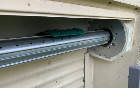 Détail du mécanisme d'un volet roulant, prêt pour comment démonter un moteur de volet roulant. Le tube métallique est visible, avec un support vert.