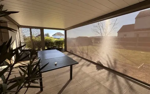Terrasse avec table et chaises, sous un abri moderne. La menuiserie RAL 7006 s'intègre parfaitement au paysage.