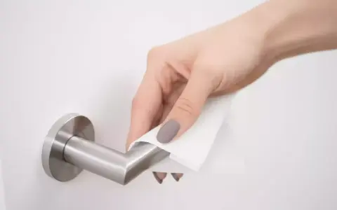 Main d'une femme nettoyant une poignée de porte en métal avec un chiffon. Apprenez comment nettoyer poignée métal vieilli pour lui redonner son éclat.