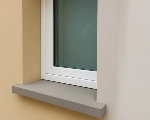 Une pose fenêtre sur appui de fenêtre en pierre grise, avec un mur extérieur texturé beige et un mur blanc cassé.