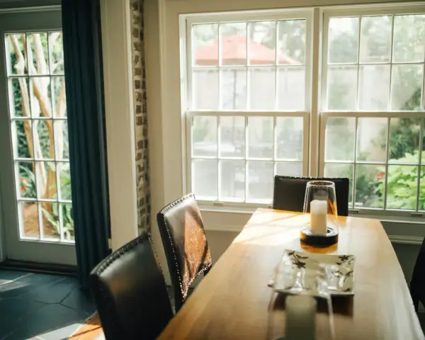 Le **couleur encadrement fenêtre intérieur** blanc met en valeur la lumière naturelle baignant la salle à manger. Des chaises en cuir marron entourent une table en bois.