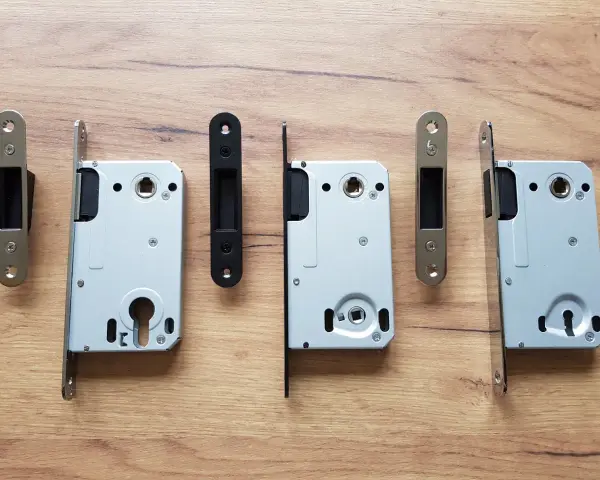 Ensemble de serrures pour porte intérieure, avec leurs gâches argentées et noires, sur fond de bois.