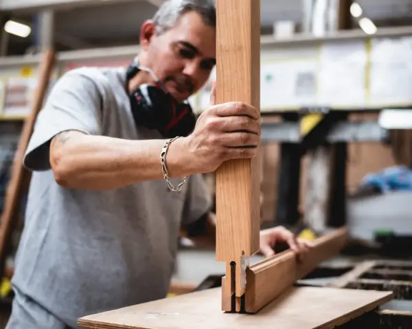 Artisan assemble des pièces de bois pour fabriquer une fenêtre. Il tient une pièce verticale et la joint à une autre pièce.