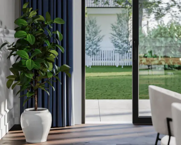 Vue sur jardin verdoyant depuis une pièce, avec un ficus en pot près du détail seuil porte fenêtre.