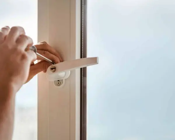 Main tenant utilise un tournevis pour changer la poignée d'une fenêtre en aluminium.