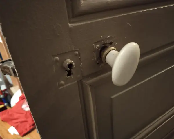 Détail du mécanisme poignée porte ancienne avec une rosace et une serrure visible.