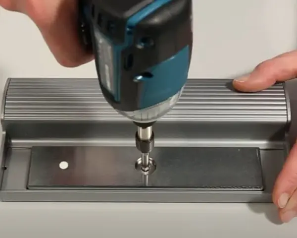 Utilisation d'une visseuse pour fixer une plaque métallique, étape clé pour ouvrir une porte aimantée.