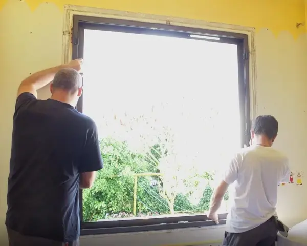 Deux hommes installent une nouvelle fenêtre, une étape clé dans la rénovation de cette pièce.