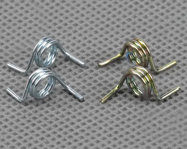 Deux ressorts argentés et deux ressorts dorés, essentiels au mécanisme d'une serrure de portail, reposent sur une surface texturée.
