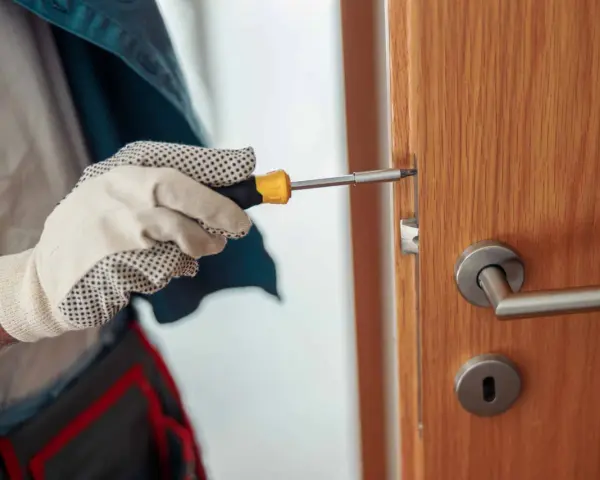 Main tenant utilise un tournevis pour réparer une serrure qui coince sur une porte en bois.