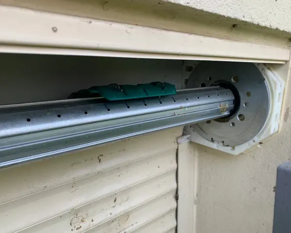 Détail du mécanisme d'un volet roulant, prêt pour comment démonter un moteur de volet roulant. Le tube métallique est visible, avec un support vert.