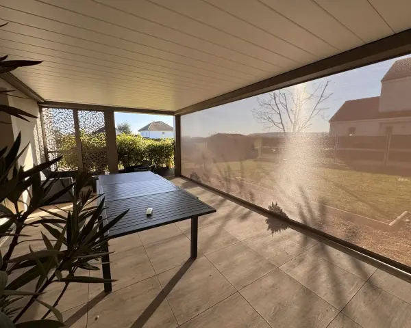 Terrasse avec table et chaises, sous un abri moderne. La menuiserie RAL 7006 s'intègre parfaitement au paysage.