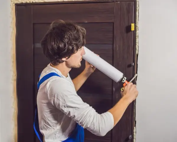 Un homme utilise une mousse expansive pour isoler une porte en bois.