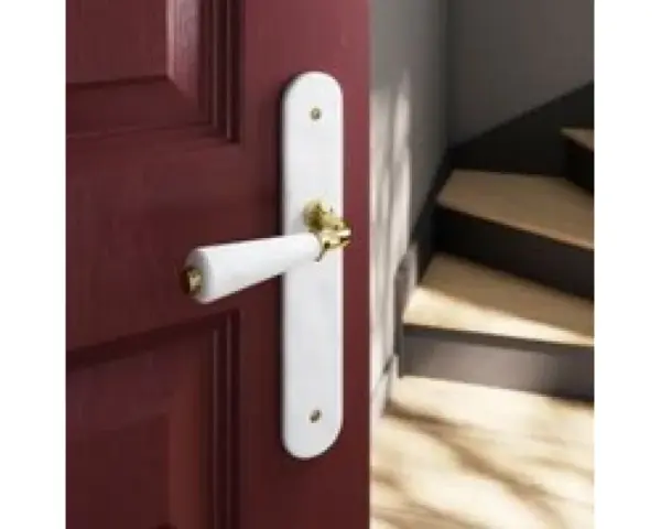 Poignée de porte blanche sur fond bordeaux, avec un escalier en bois visible. Quelle couleur de poignée pour porte blanche ? L'or brille.