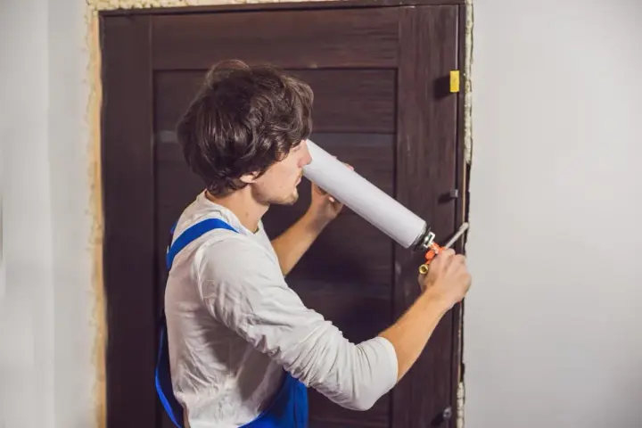 Un homme utilise une mousse expansive pour isoler une porte en bois.