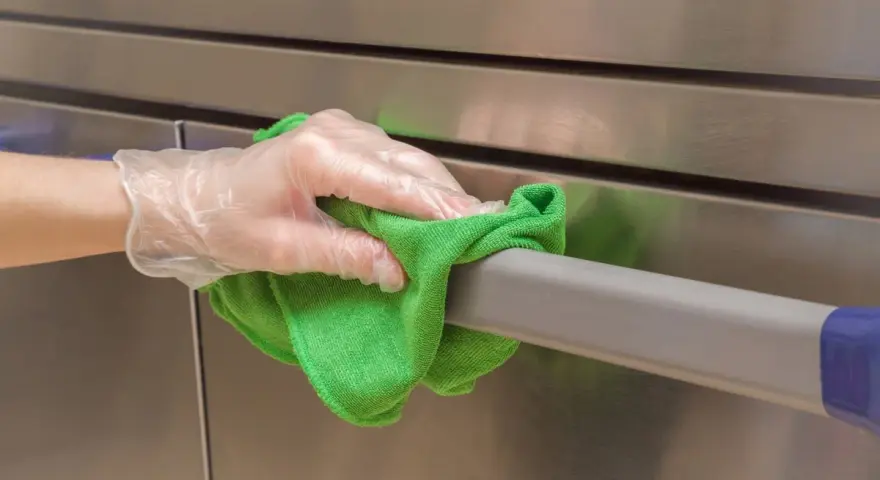 Main tenant nettoie avec un chiffon vert un acier inoxydable doré, gardant une hygiène impeccable.