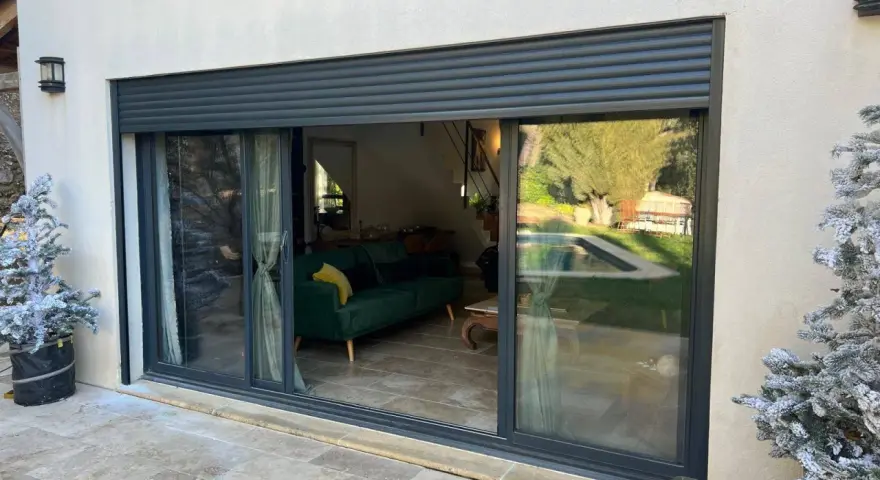 Volet battant alu RAl 7016, moderne, protégeant une baie vitrée donnant sur un salon et une piscine.