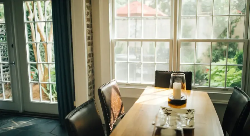Le **couleur encadrement fenêtre intérieur** blanc met en valeur la lumière naturelle baignant la salle à manger. Des chaises en cuir marron entourent une table en bois.