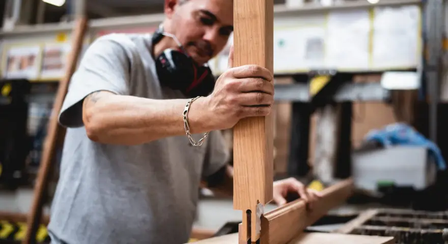 Artisan assemble des pièces de bois pour fabriquer une fenêtre. Il tient une pièce verticale et la joint à une autre pièce.