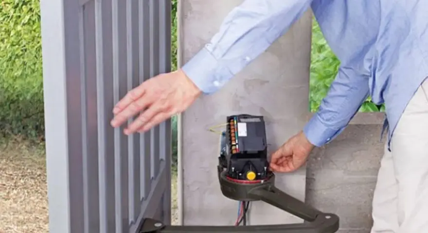Un homme ajuste le moteur d'un portail électrique bloqué ouvert.