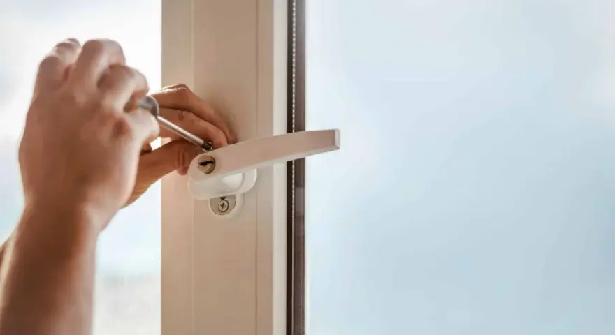 Main tenant utilise un tournevis pour changer la poignée d'une fenêtre en aluminium.