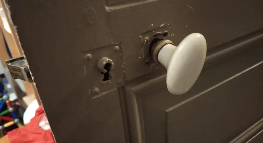 Détail du mécanisme poignée porte ancienne avec une rosace et une serrure visible.