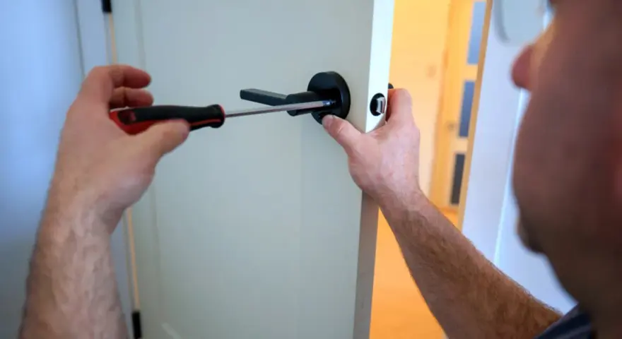 Un homme utilise un tournevis pour fixer une poignée de porte noire. Il est sur le point de lever la poignée pour fermer la porte.