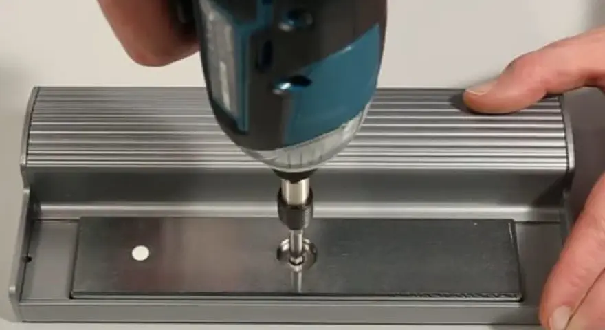 Utilisation d'une visseuse pour fixer une plaque métallique, étape clé pour ouvrir une porte aimantée.