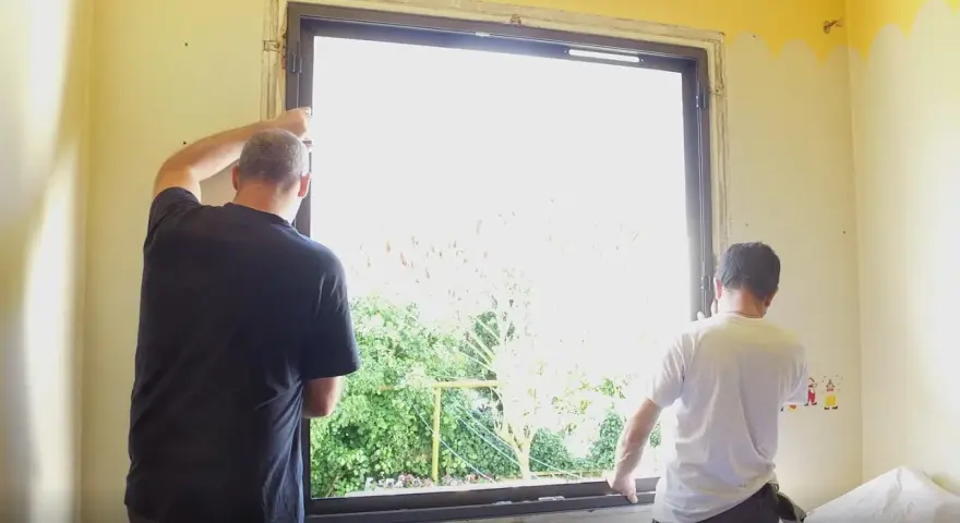 Deux hommes installent une nouvelle fenêtre, une étape clé dans la rénovation de cette pièce.