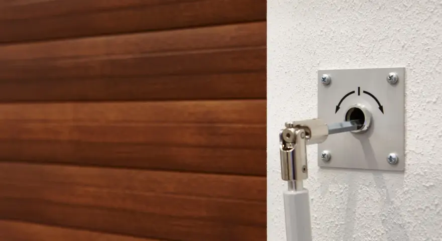 Mécanisme pour comment ouvrir une porte de garage électrique de l'extérieur. Un levier est inséré dans une serrure sur un mur blanc, à côté d'une porte en bois.