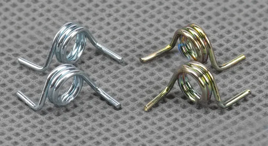 Deux ressorts argentés et deux ressorts dorés, essentiels au mécanisme d'une serrure de portail, reposent sur une surface texturée.