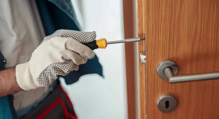 Main tenant utilise un tournevis pour réparer une serrure qui coince sur une porte en bois.